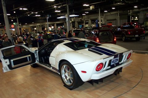 2001 Ford Crown Victoria - A white Ford GT with blue racing stripes is displayed indoors with its driver's door open.