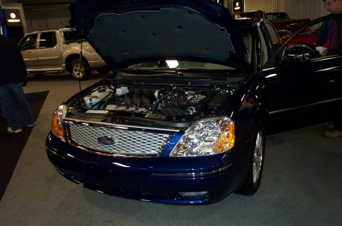 2001 Ford Crown Victoria - A blue sedan is displayed with its hood open, revealing the engine and front grille. Another vehicle is visible in the background.