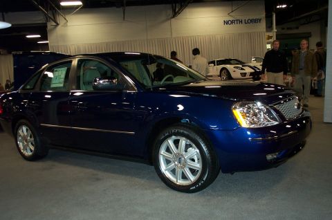 2001 Ford Crown Victoria - A dark blue sedan is displayed indoors next to a white sports car.