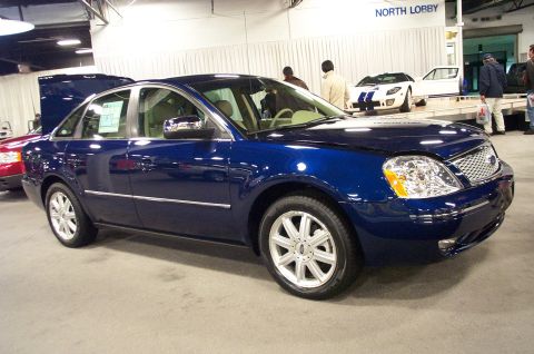 2001 Ford Crown Victoria - A blue sedan is displayed indoors, with a white Ford GT visible behind it.