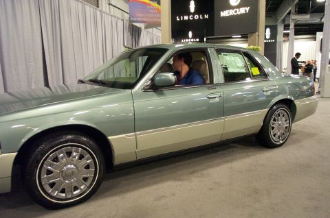 2001 Ford Crown Victoria - A two-tone Mercury Grand Marquis is displayed at an auto show with Lincoln and Mercury branding visible.