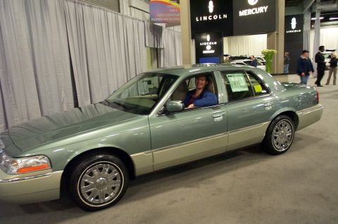 2001 Ford Crown Victoria - A man sits in a two-tone sedan at what appears to be an auto show.