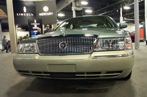 2001 Ford Crown Victoria - A light green Mercury Grand Marquis is displayed at an auto show, with Lincoln and Mercury branding visible behind it.