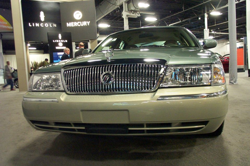 Front view of a light green Mercury Grand Marquis with a chrome grille and Lincoln/Mercury signage in background