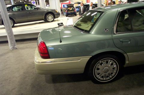2001 Ford Crown Victoria - A light green Mercury Grand Marquis is shown from the rear quarter, with a gray sedan in the background at an auto show.