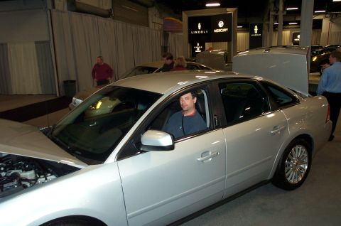 2001 Ford Crown Victoria - A silver sedan is displayed with its hood open, while a man sits in the driver's seat.