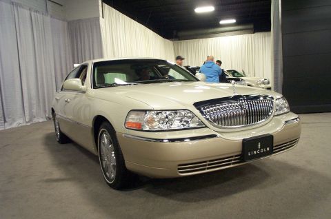 2001 Ford Crown Victoria - A cream and tan Lincoln Town Car is displayed indoors with other vehicles visible in the background.
