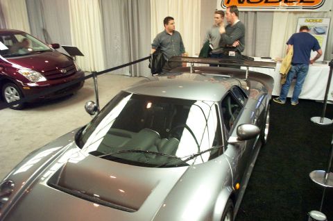 2001 Ford Crown Victoria - A silver sports car with a prominent rear spoiler is displayed indoors, with another car visible in the background.
