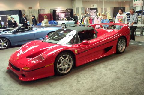 2001 Ford Crown Victoria - A red Ferrari convertible is displayed indoors, with a blue convertible parked behind it and people observing.