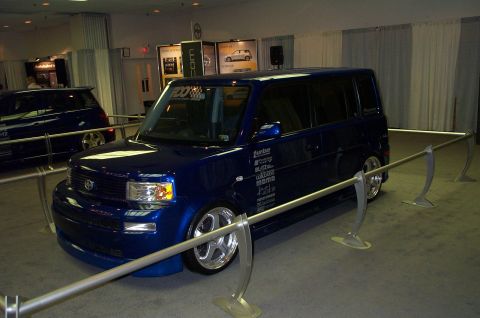 2001 Ford Crown Victoria - A blue hatchback with various performance decals is displayed indoors, with another similar vehicle visible in the background.