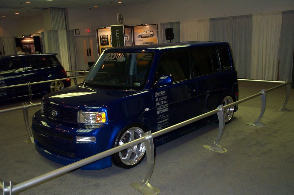 Blue hatchback car with many decals on the side, parked indoors with another car behind it