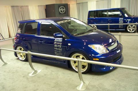 2001 Ford Crown Victoria - Modified blue hatchback with various sponsor decals and gold rims on display.