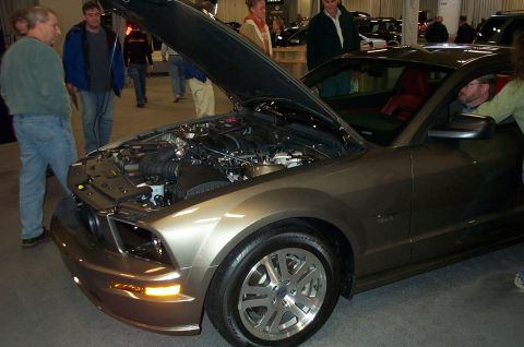 2001 Ford Crown Victoria - A man peers into the engine bay of a modern Ford Mustang at an indoor car show.