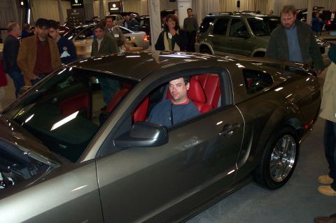 2001 Ford Crown Victoria - A man sits in a gray coupe with a red interior at an auto show.