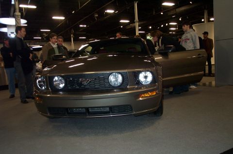 2001 Ford Crown Victoria - A Ford Mustang is displayed indoors with its door open, attracting attention from onlookers.