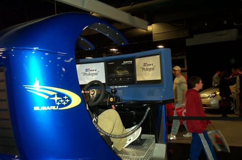 2001 Ford Crown Victoria - A Subaru racing simulator setup is displayed with multiple screens and a steering wheel, promoting Gran Turismo 4 Prologue.