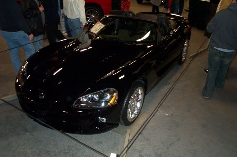 2001 Ford Crown Victoria - A black convertible sports car is displayed indoors with people around.