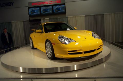 2001 Ford Crown Victoria - A bright yellow Porsche 911 is showcased on a rotating platform, with the PORSCHE logo visible in the background.