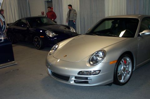 2001 Ford Crown Victoria - Two Porsche 911s are displayed indoors, with two men standing nearby.