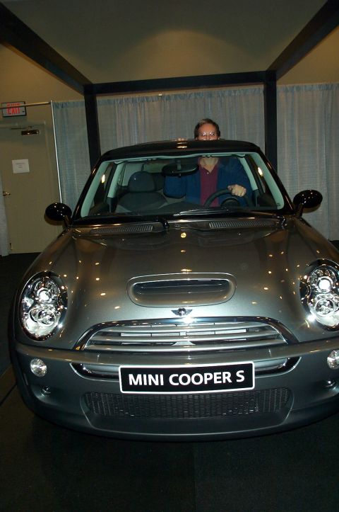 2001 Ford Crown Victoria - A person peeks over the windshield of a gray Mini Cooper S. The car has a 'MINI COOPER S' badge on the front.