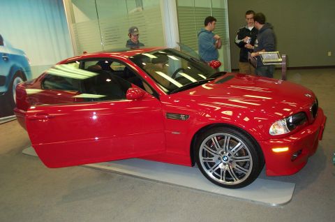 2001 Ford Crown Victoria - A red BMW coupe is displayed with its driver's door open, attracting attention from onlookers.