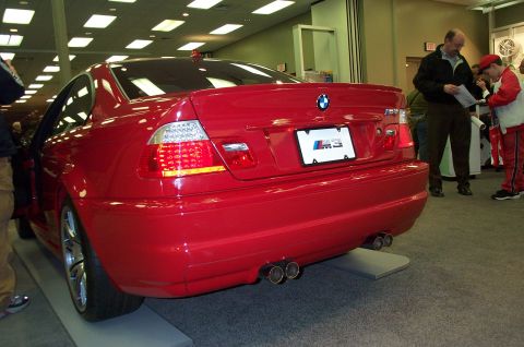 2001 Ford Crown Victoria - A red BMW M3 coupe is displayed indoors, showing its rear end with distinctive M3 badging and quad exhaust pipes.