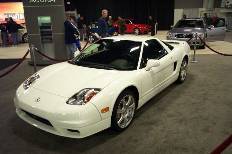 2001 Ford Crown Victoria - A white sports car is displayed indoors with other vehicles and attendees.