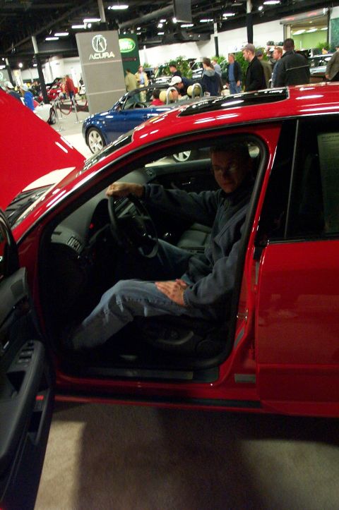 2001 Ford Crown Victoria - A man sits in the driver's seat of a red car with the door open at an auto show.
