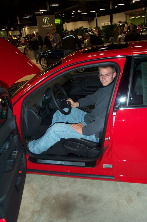2001 Ford Crown Victoria - A man sits in the driver's seat of a red sedan, which appears to be on display at an auto show.