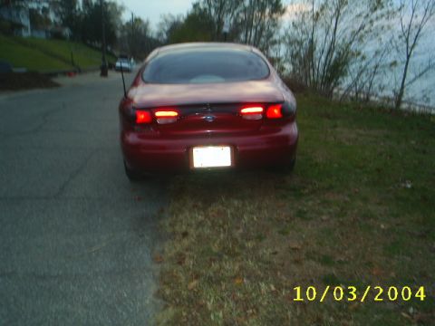 1997 Ford Taurus - A red 1997 Ford Taurus is parked on the side of a road with a body of water in the background.