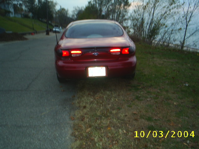 Red 1997 Ford Taurus parked on the side of a road near water, rear view