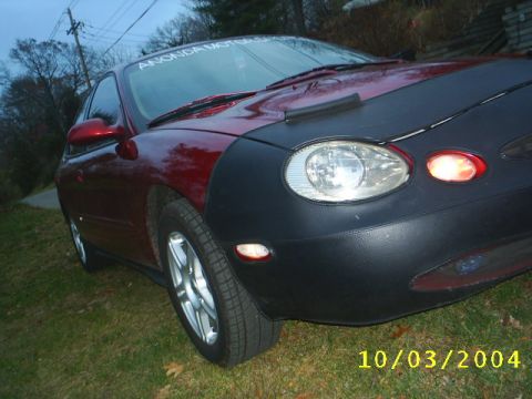 1997 Ford Taurus - A red car is partially covered by a black car bra, obscuring its front end. The photo was taken on October 3, 2004.