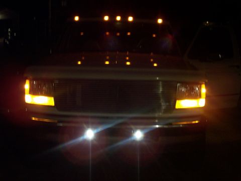1994 Ford Bronco - Front view of a white Ford truck at night, showing its illuminated headlights and turn signals.