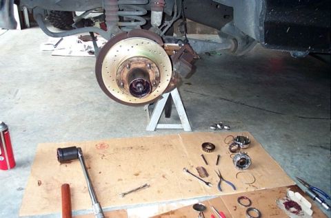 1995 Ford Bronco - Front brake assembly and associated parts are laid out on the floor for maintenance.