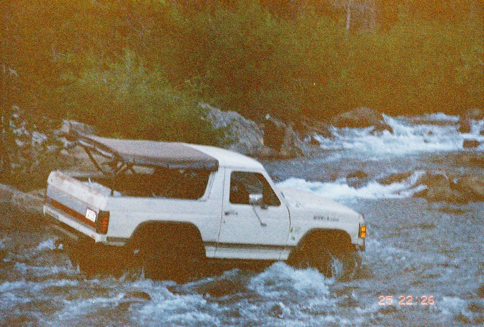 White Ford Bronco with soft top in river, front quarter view