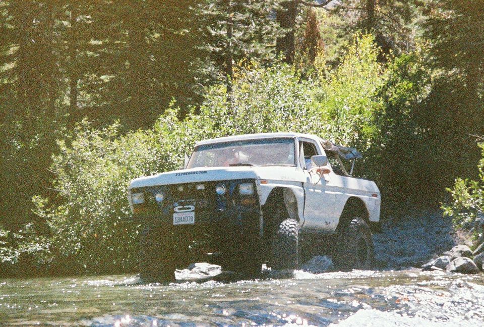 White lifted 4x4 crossing a rocky forest creek on oversized mud tires with light bar
