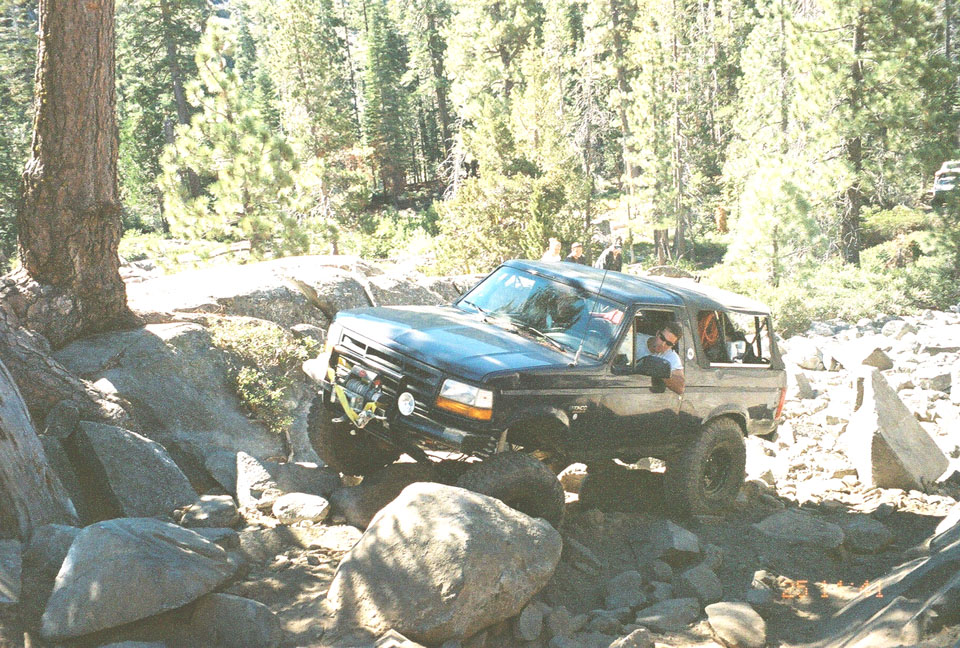 Dark green topless Ford Bronco with winch bumper crawling over granite boulders