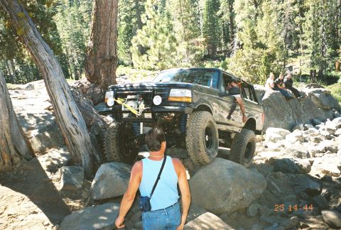 1994 Ford Bronco - A black 1994 Ford Bronco tackles a challenging rocky trail with people watching from a boulder.