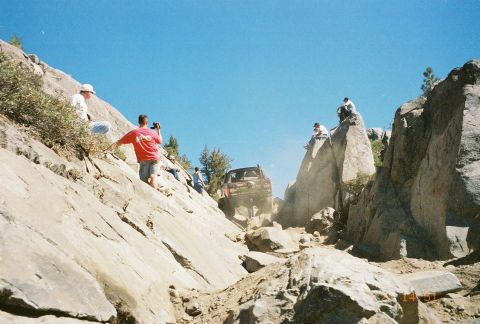 1994 Ford Bronco - A black SUV navigates a steep, rocky terrain with onlookers observing from the sides.