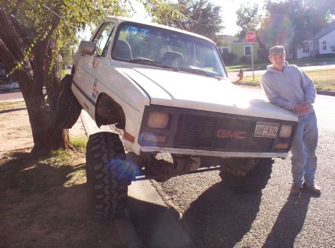 1988 Ford Bronco - A white GMC pickup truck is parked with its front tire lodged in a tree, while a young man stands nearby.