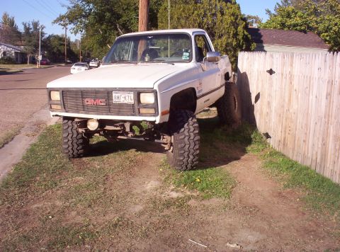 1988 Ford Bronco - This lifted GMC pickup truck is parked on grass next to a wooden fence. The license plate is visible.