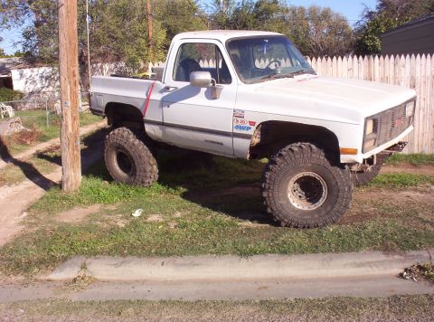 1988 Ford Bronco - This lifted GMC pickup truck is parked on a residential street with a white picket fence in the background.