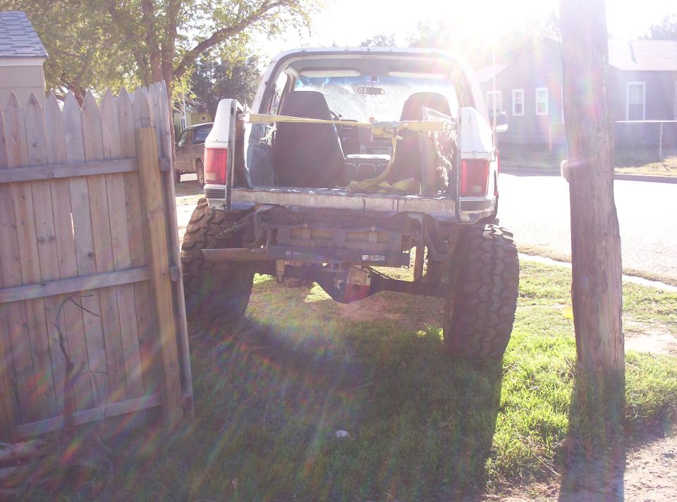 Rear of a lifted white SUV on knobby tires with tailgate down and yellow ratchet straps
