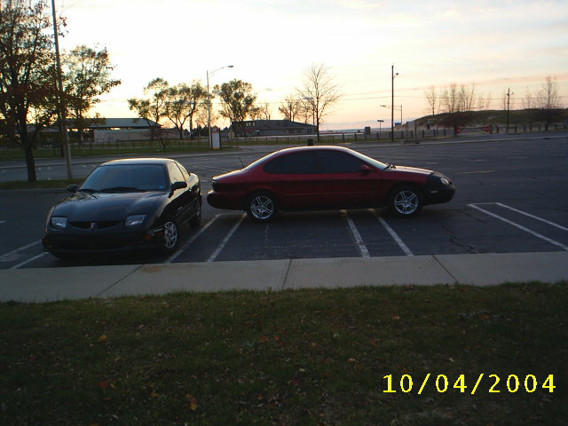 Red sedan parked next to a black car in a parking lot at dusk