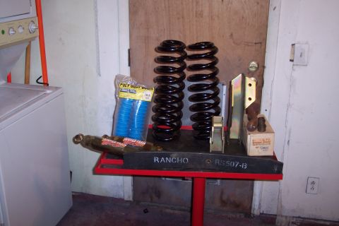 1990 Ford Bronco - Various automotive suspension components are displayed on a stand in a garage setting.