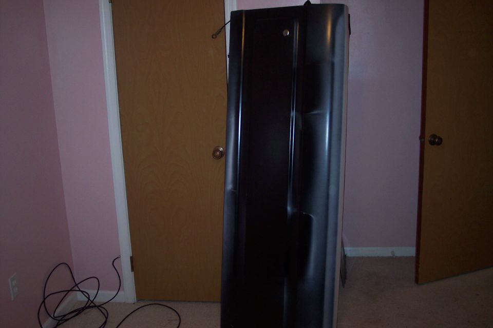 Stripped truck tailgate in dark primer standing on end indoors