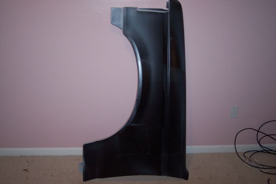 Truck front fender in dark primer standing against a pink wall, outer side showing