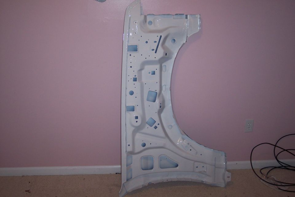 White-painted truck front fender standing against a pink wall, inner side showing