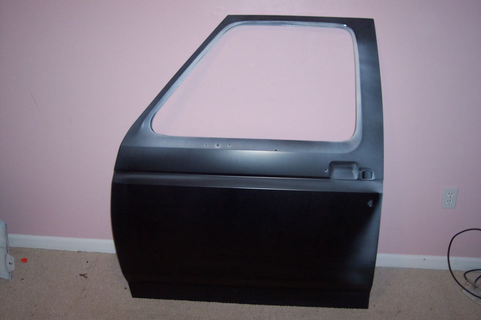 Bare truck door in dark primer standing against a pink wall, no glass or handle