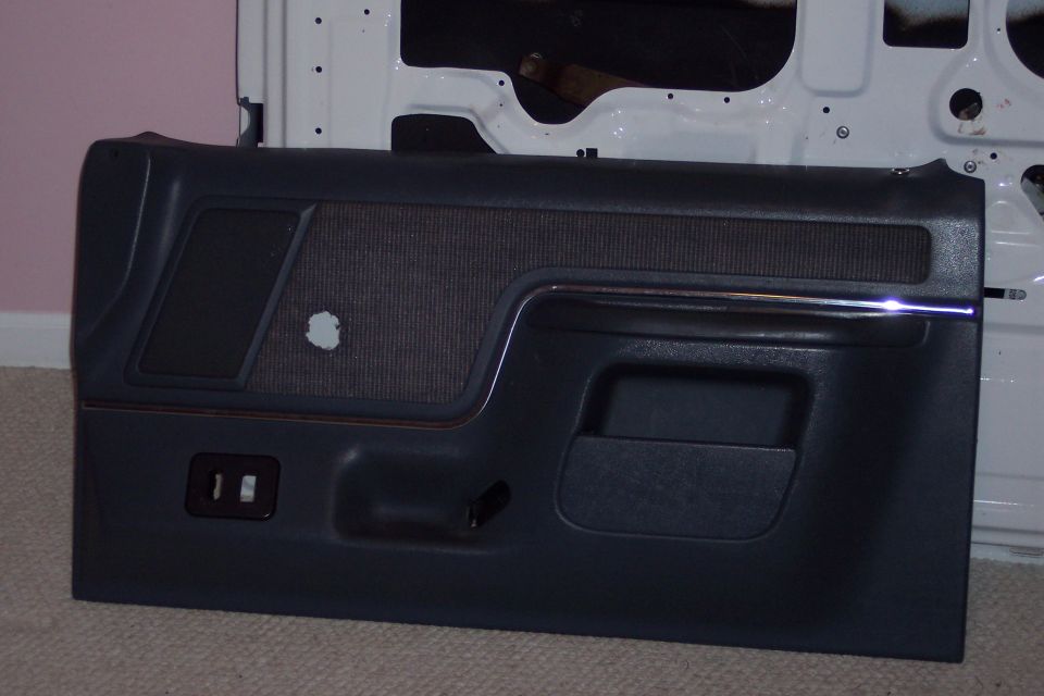 Gray truck door panel with carpet insert and armrest leaning against a white door shell